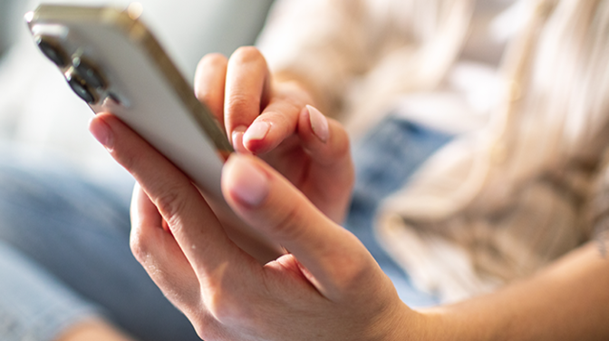 Nahaufnahme eines Smartphones, das von einer Frau festgehalten und bedient wird