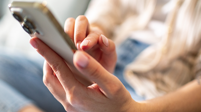 Nahaufnahme eines Smartphones, das von einer Frau festgehalten und bedient wird